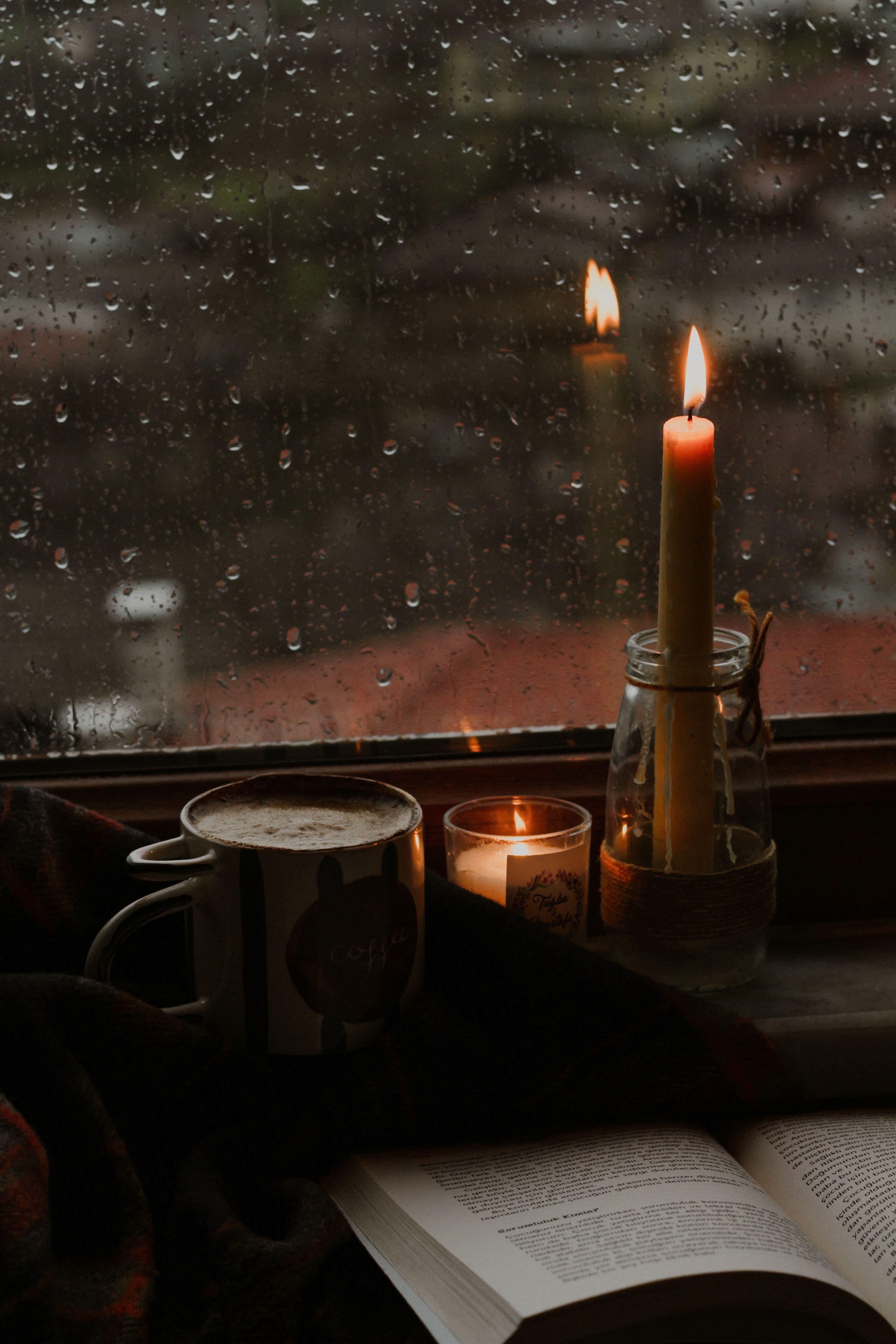 A cozy rainy-day reading nook with warm candlelight, a cup of coffee, and an open book